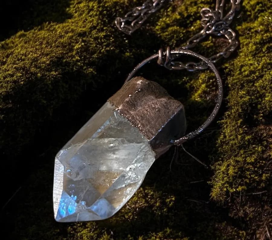 Clear quartz crystal point capped in electroformed copper on a chain, resting on moss