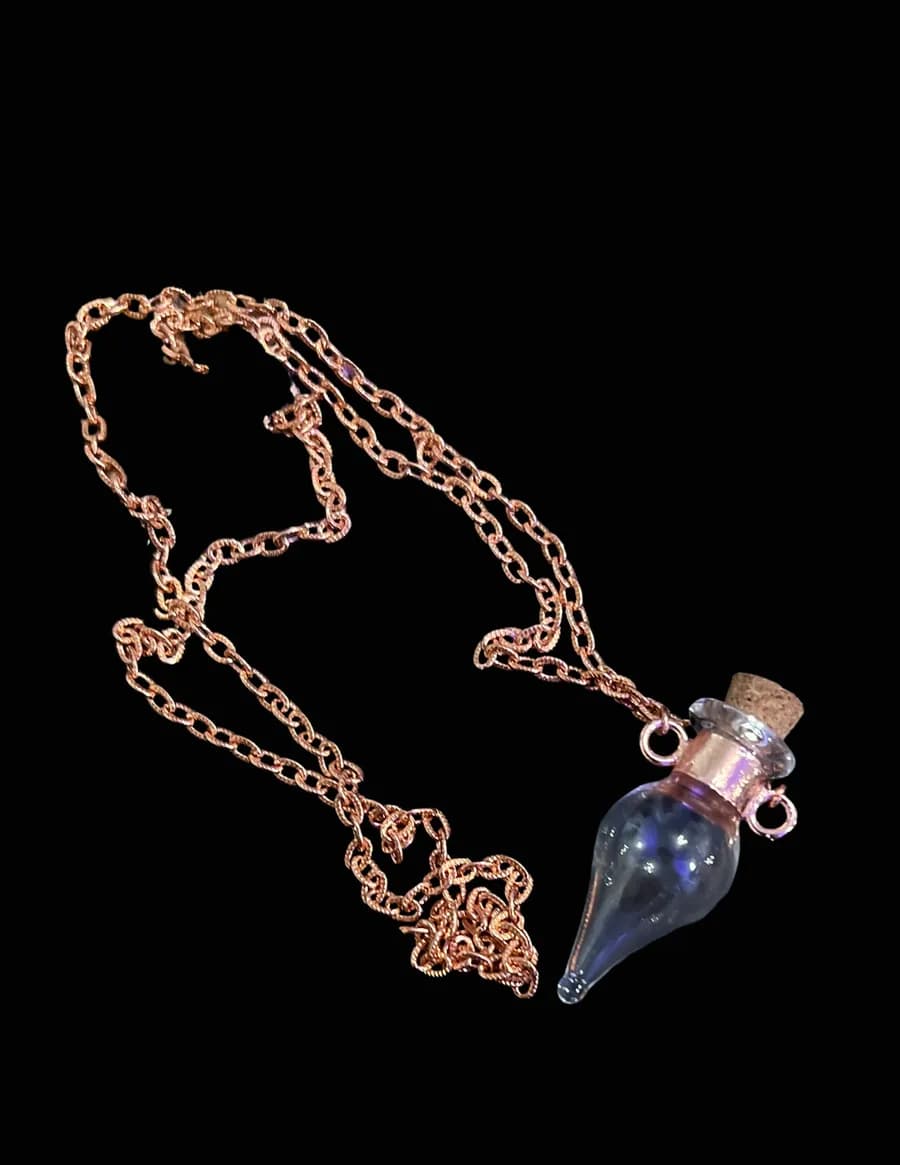 Bright copper chain necklace with a small corked glass vial pendant on a black background
