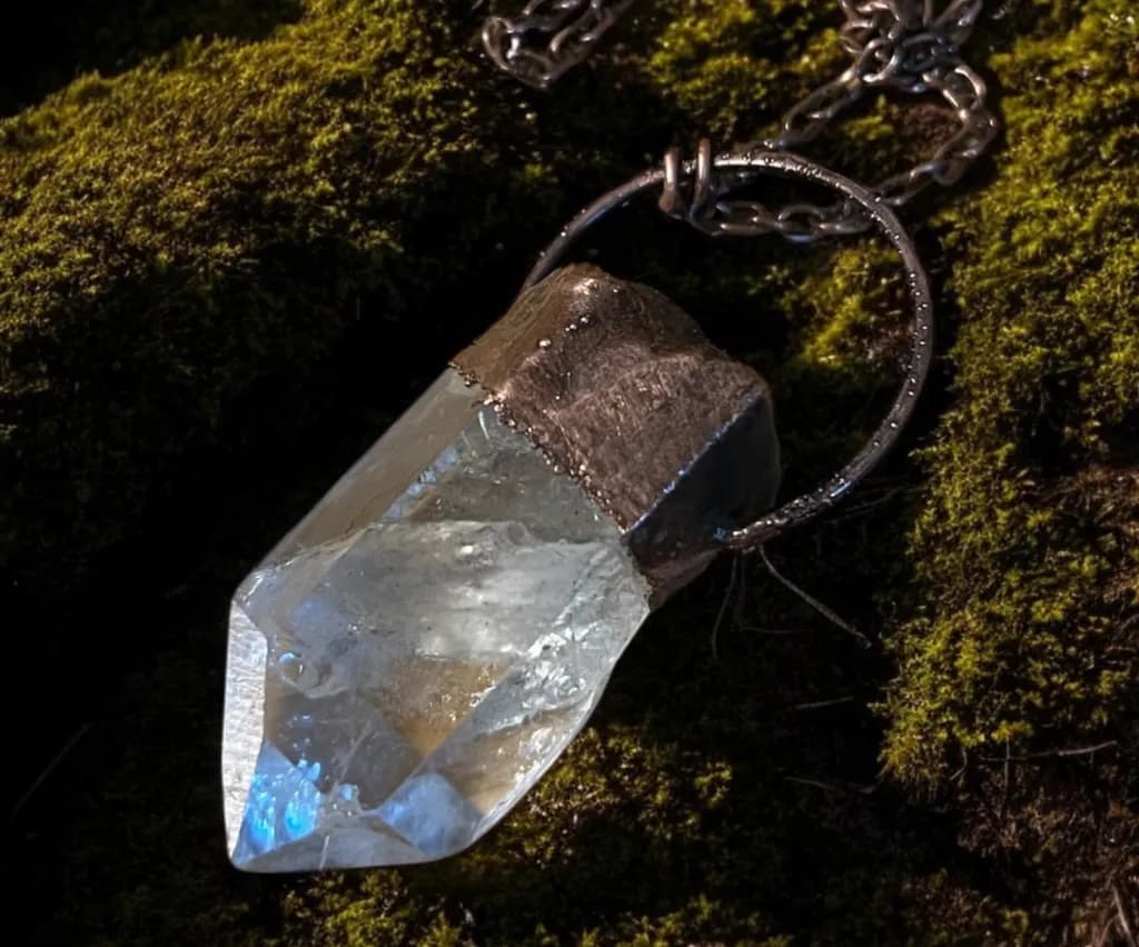 Clear quartz crystal capped in electroformed copper on a chain, resting on moss